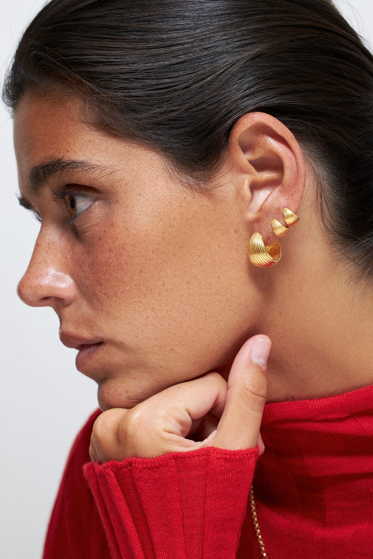 Tilly Huggie Earrings comfortable everyday wear present worn by a model with a red sweater, showcasing their elegant design.