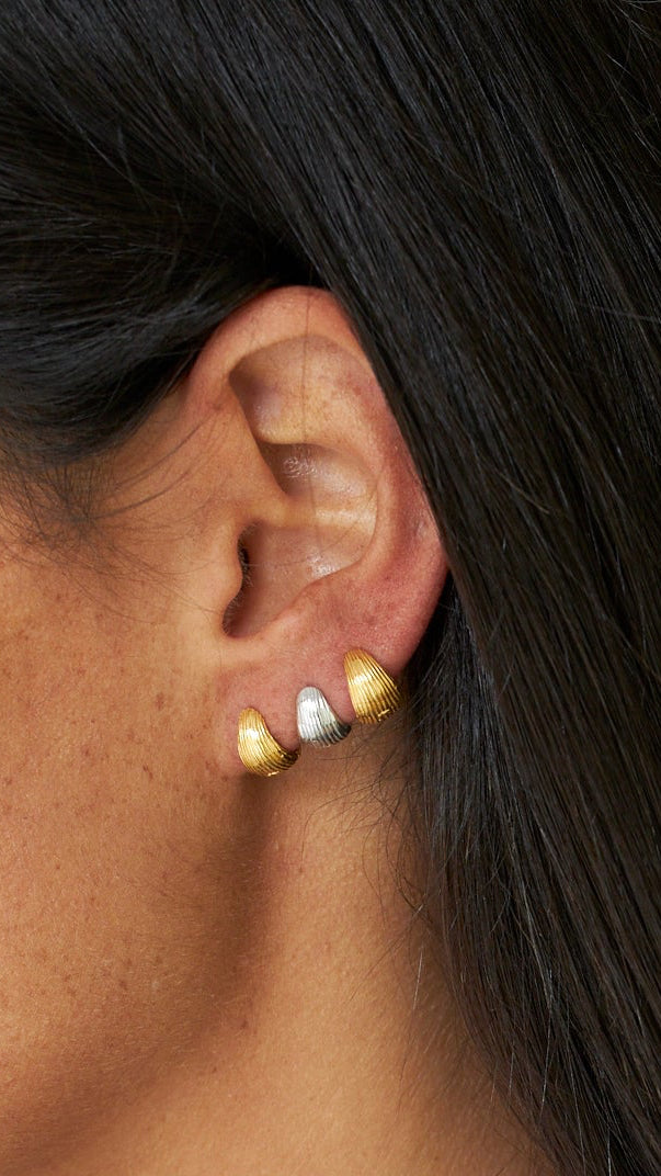 Close-up de uma orelha a usar brincos de ouro com fundo neutro