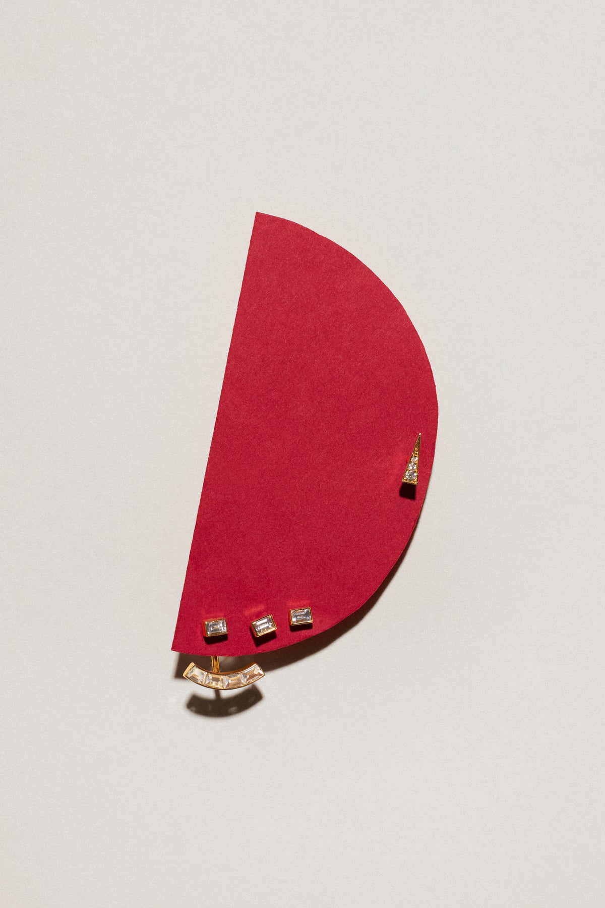 Minimalist 18ct solid gold ear piercings displayed on a red paper background, showcasing elegant designs.