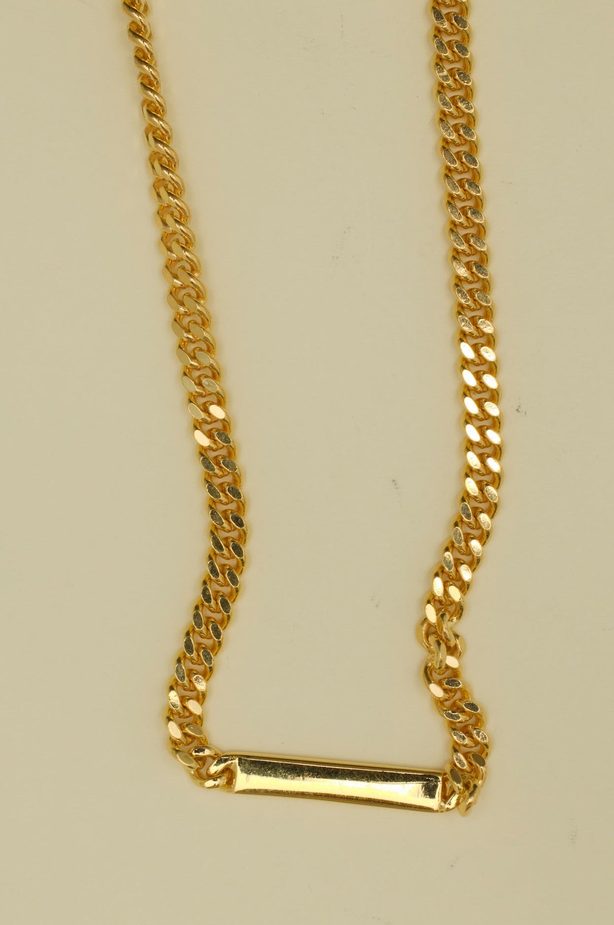 Gold chain necklace with a rectangular pendant on a beige background