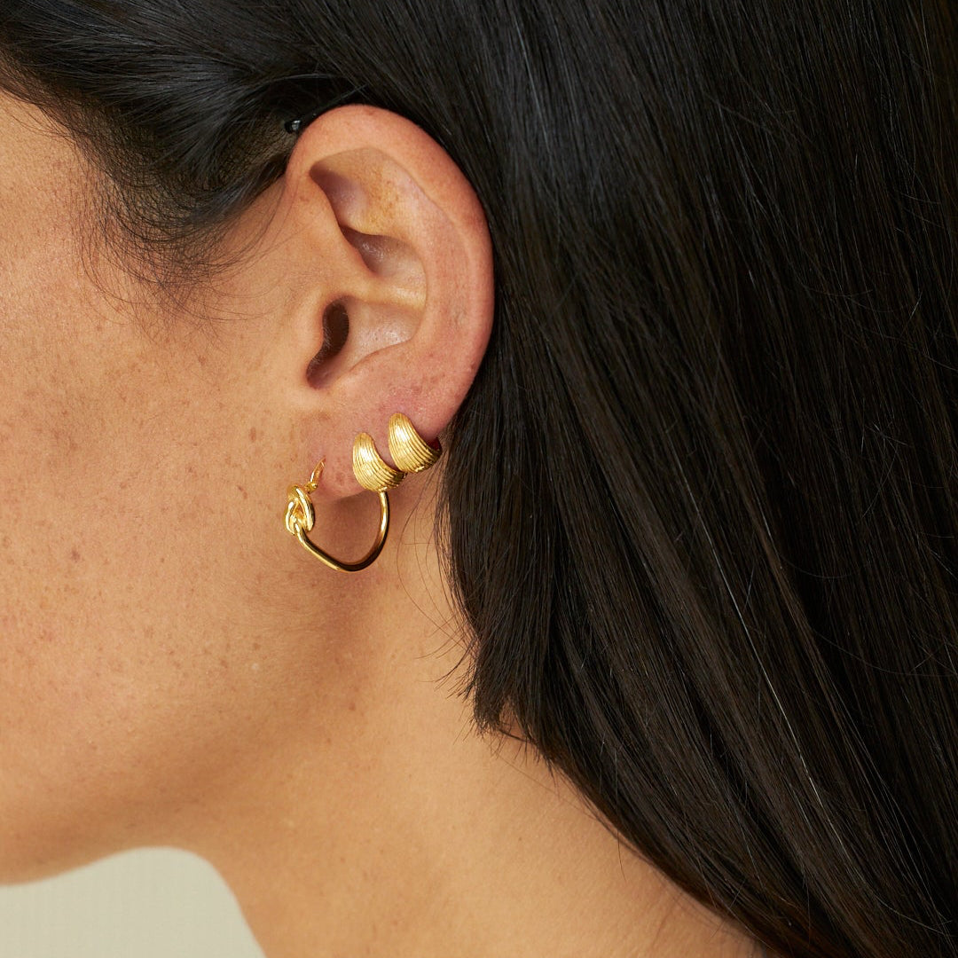 Close-up of a person wearing gold hoop earrings and a necklace.