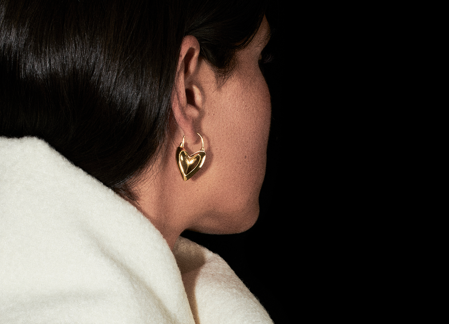 Miu huggies heart shaped earrings with a black background and winter coat.