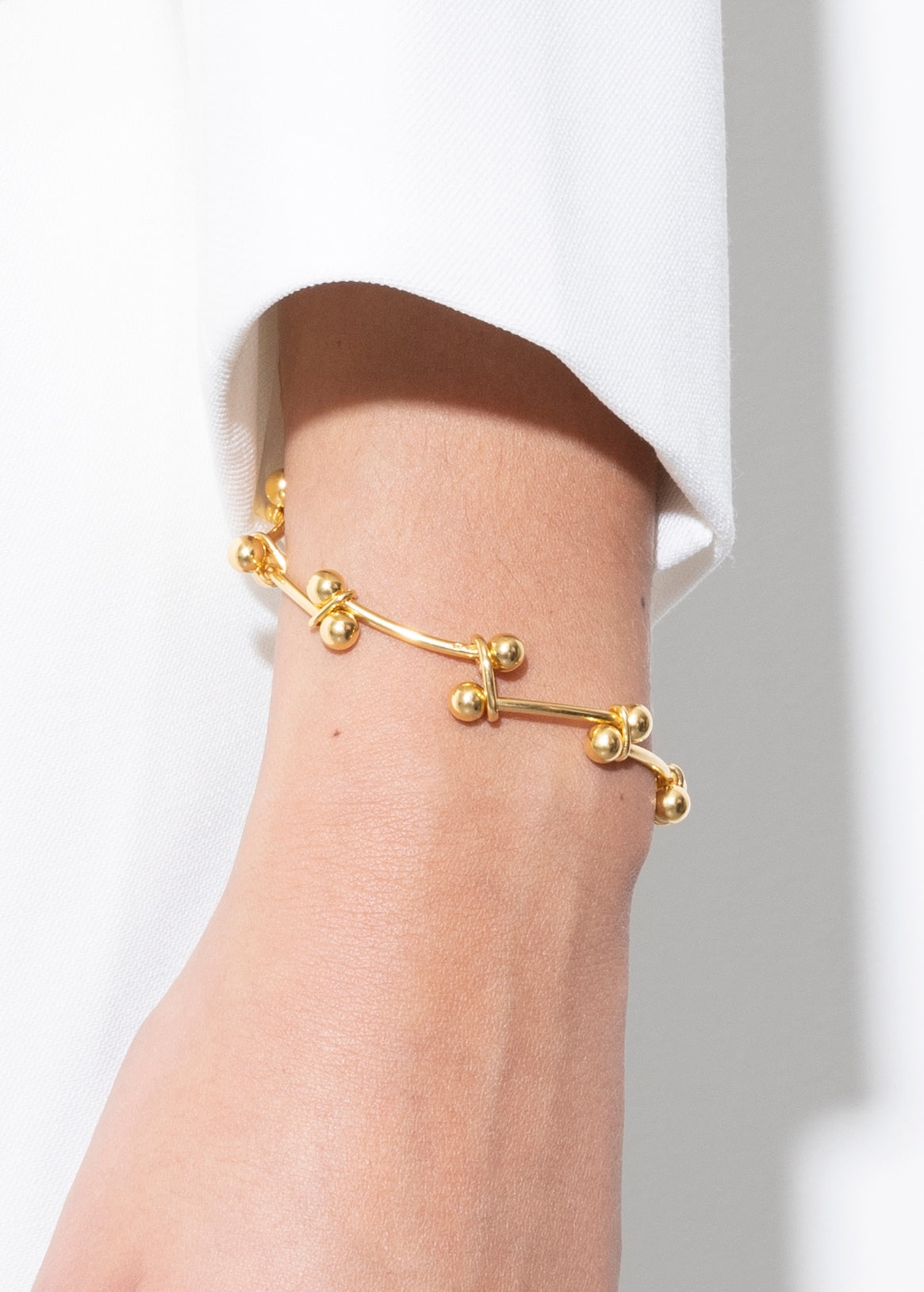 Gold bracelet on a wrist with a white background