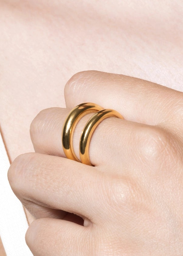 Gold ring on a finger against a light pink background