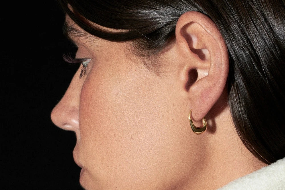 Close-up of a person wearing gold hoop earrings against a black background