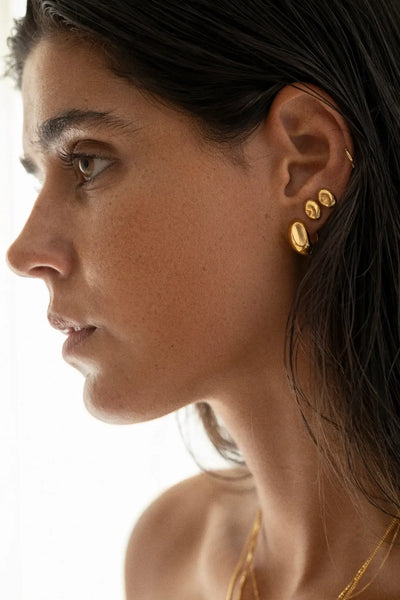 Close-up de uma mulher a usar brincos de ouro com fundo neutro