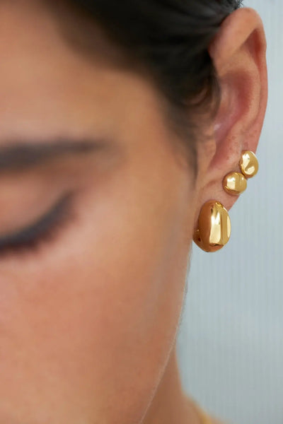 Close-up de uma pessoa a usar brincos de ouro com fundo neutro