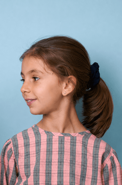 Rapazinha a usar uma camisola às riscas rosa e cinzenta contra um fundo azul