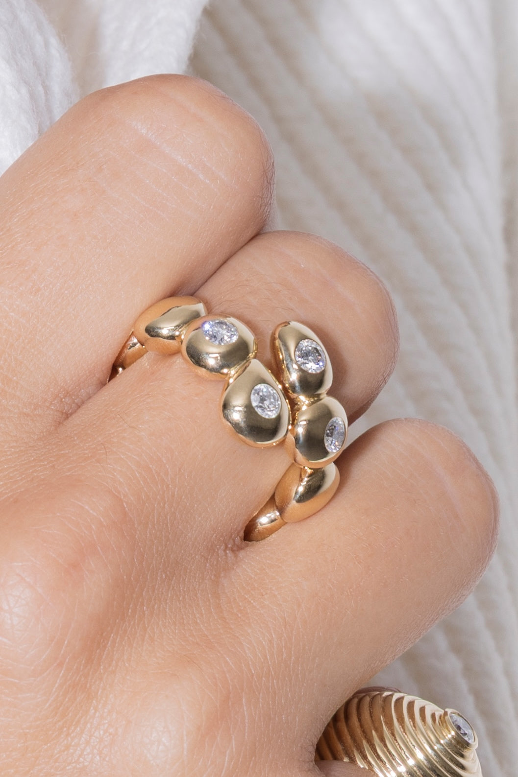 Gold ring with teardrop-shaped stones on a finger against a neutral background